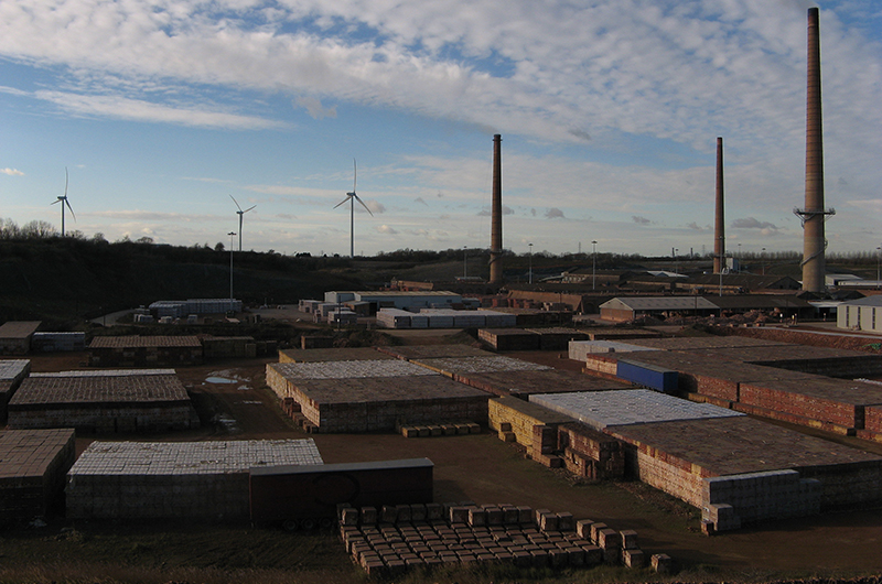 A view of a typical brick industry. Chimneys and piles of bricks are in the foreground. In the background there are wind turbines. Photo by Anna Robinson.