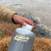 Hand holding a large beaker next to water body with the label "dairy wastewater 03/08/2022"