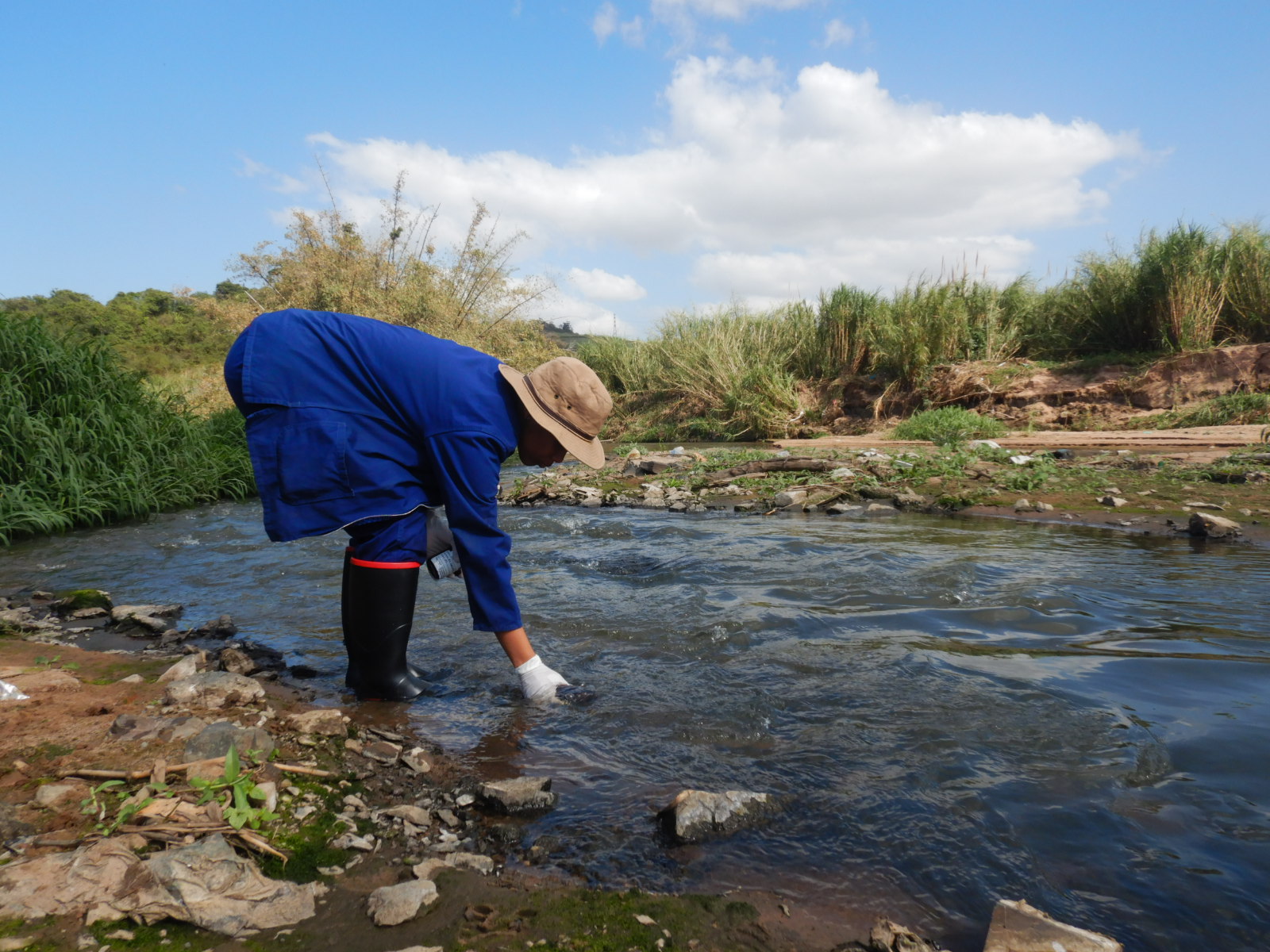Person bending down in stream to collect water 