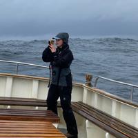Photographer of a fieldworker using a laser rangefinder on a small boat in rough sea conditions. Image courtesy of Orea Anderson