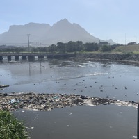 River body with litter boom filled with solid waste. Mountain in the background
